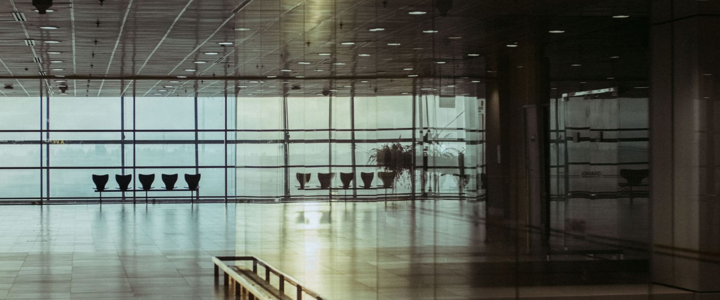 A quiet airport terminal window in soft morning light — calm, unhurried travel.